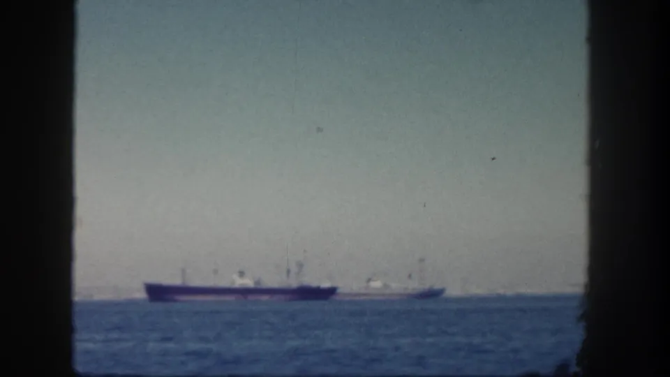 1962 San Diego home-movie view of distant cargo ships on the ocean, bordered by dark vertical frame edges.