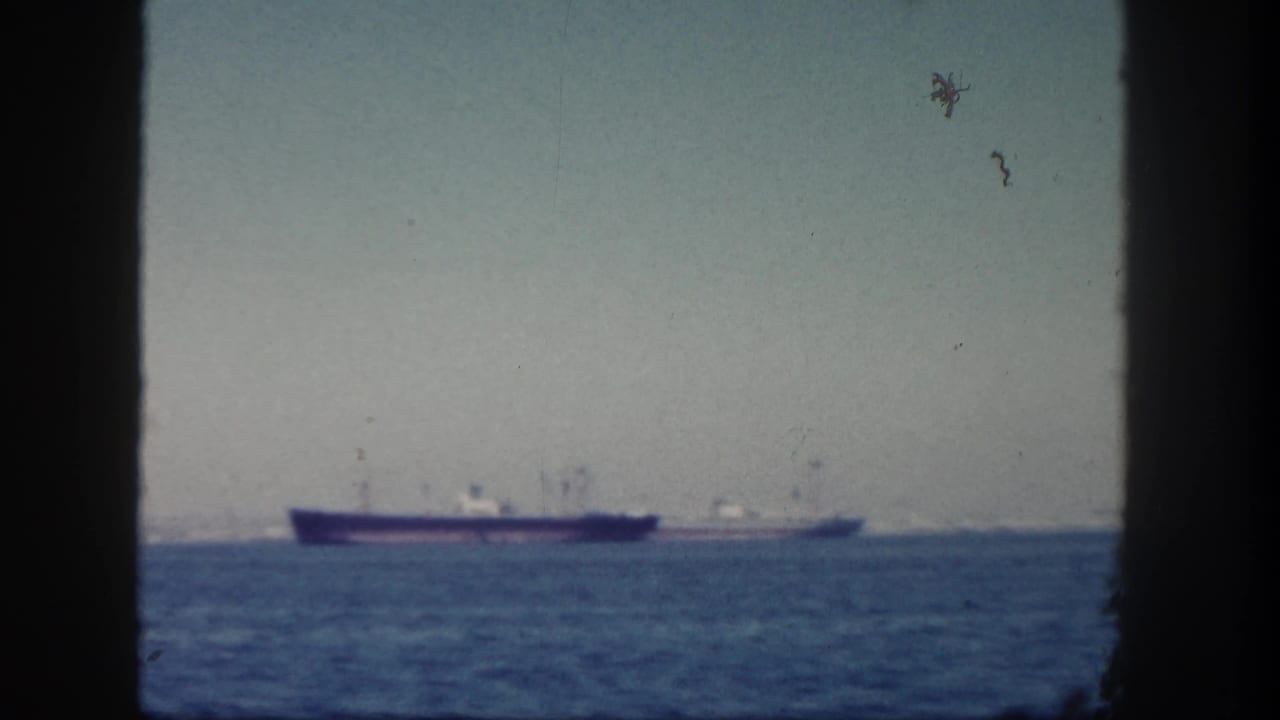 Distant ships on calm ocean water seen through a dark vessel window frame.