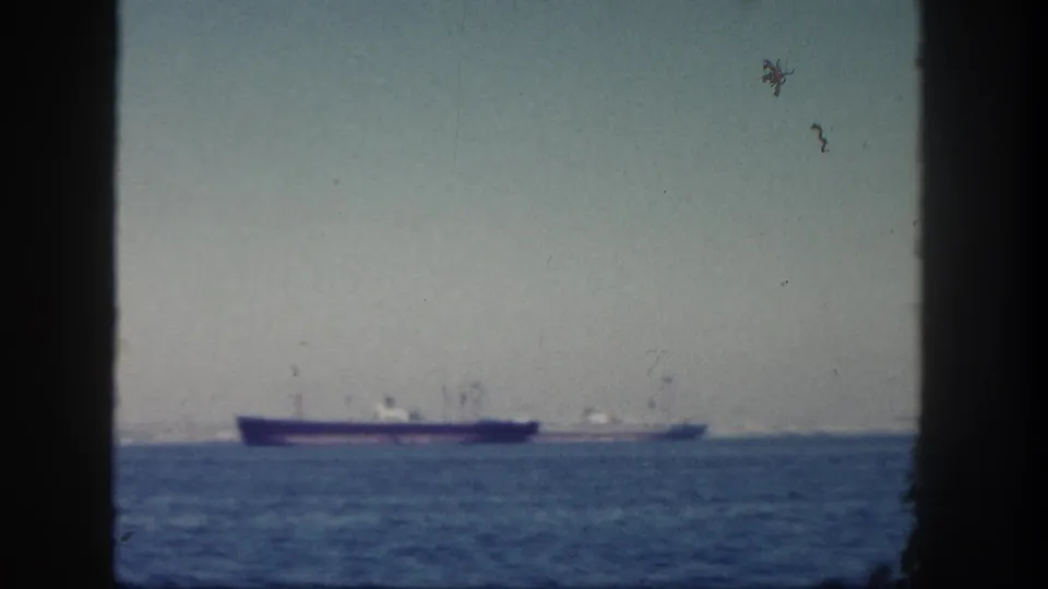 1962 San Diego home-movie view of distant ships on blue ocean water, framed by a dark window or porthole edge.