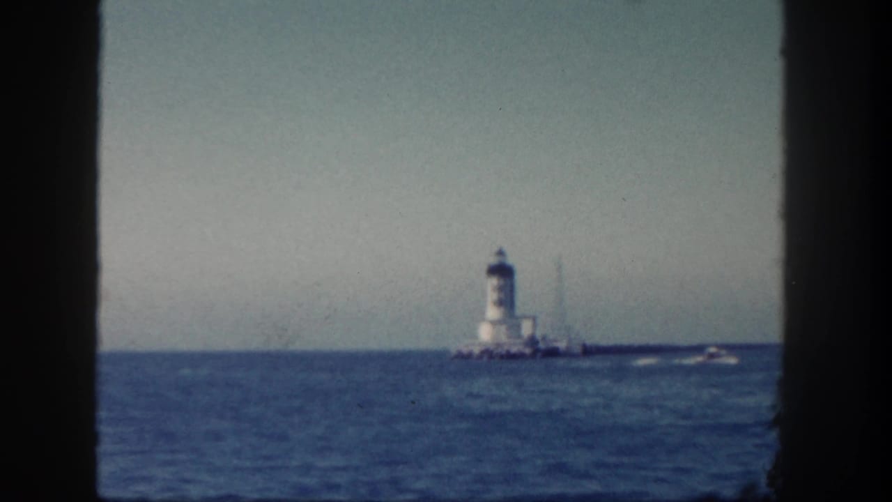 1962 San Diego maritime view of a white lighthouse in the distance with a small boat passing over blue water.
