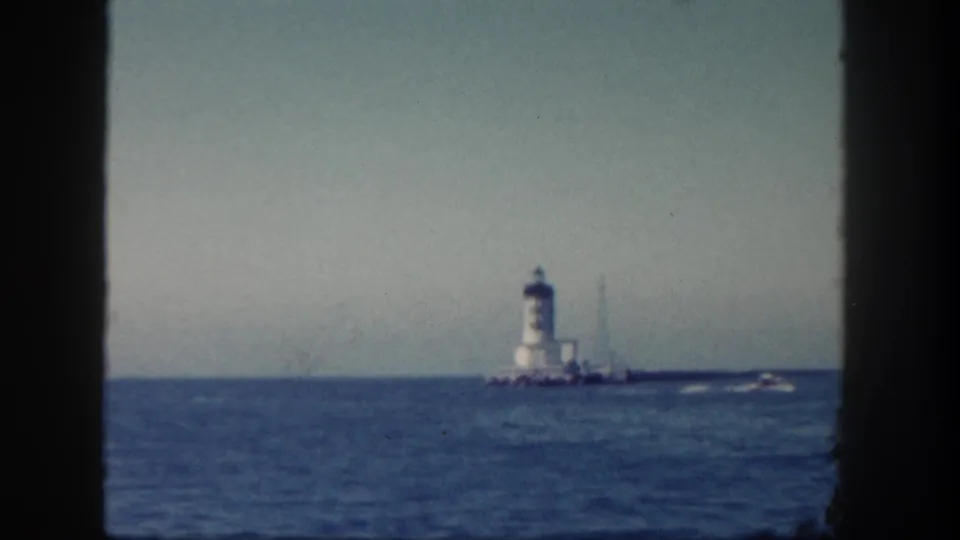 1962 San Diego maritime view of a white lighthouse in the distance with a small boat passing over blue water.