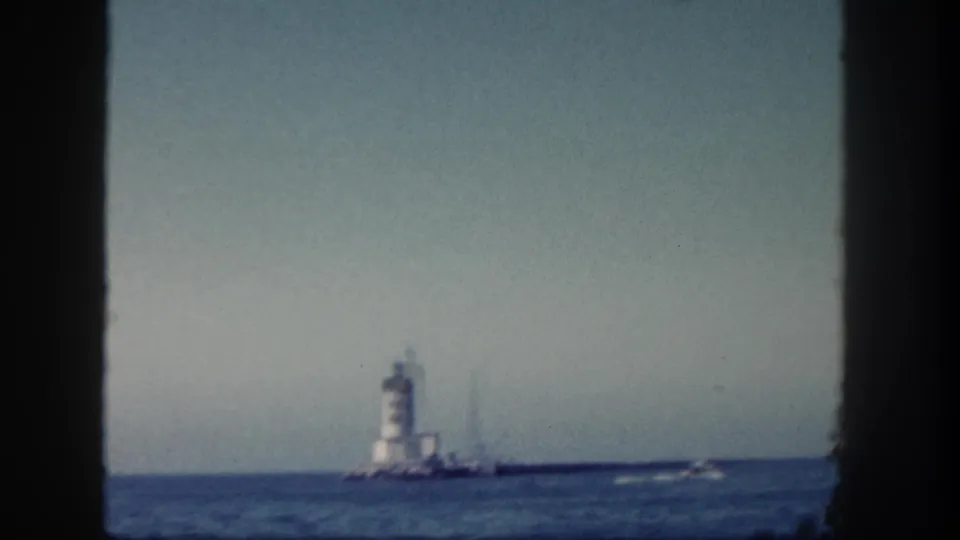 1962 San Diego home-movie frame of a distant lighthouse, low horizon, and small boat wake on blue water.