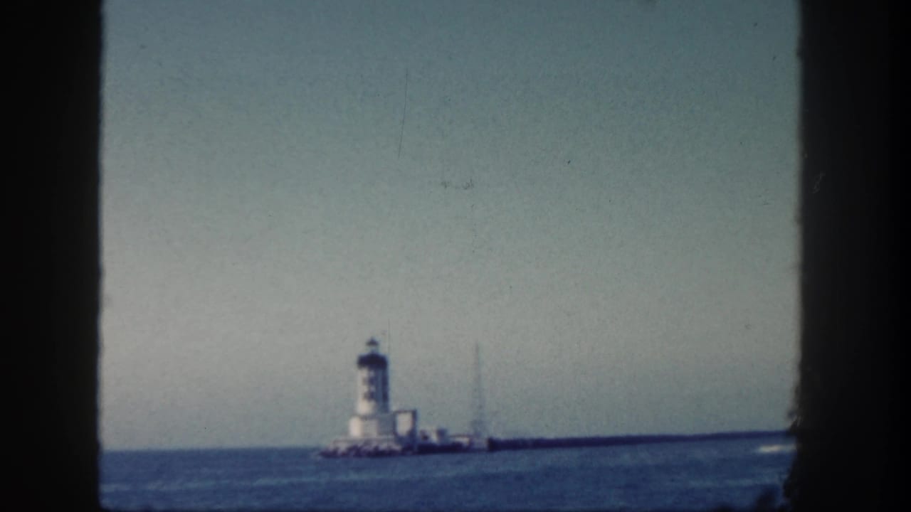 Distant San Diego waterfront view with a white tower on a long breakwater, seen through dark foreground borders.