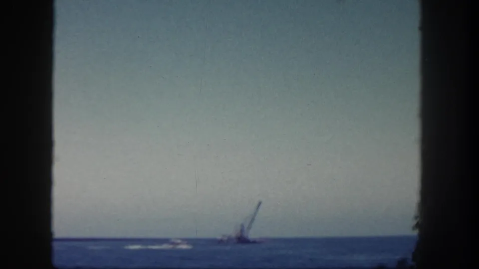 San Diego 1962 home-movie frame showing open harbor water, a small white wake, and a distant crane-like form.