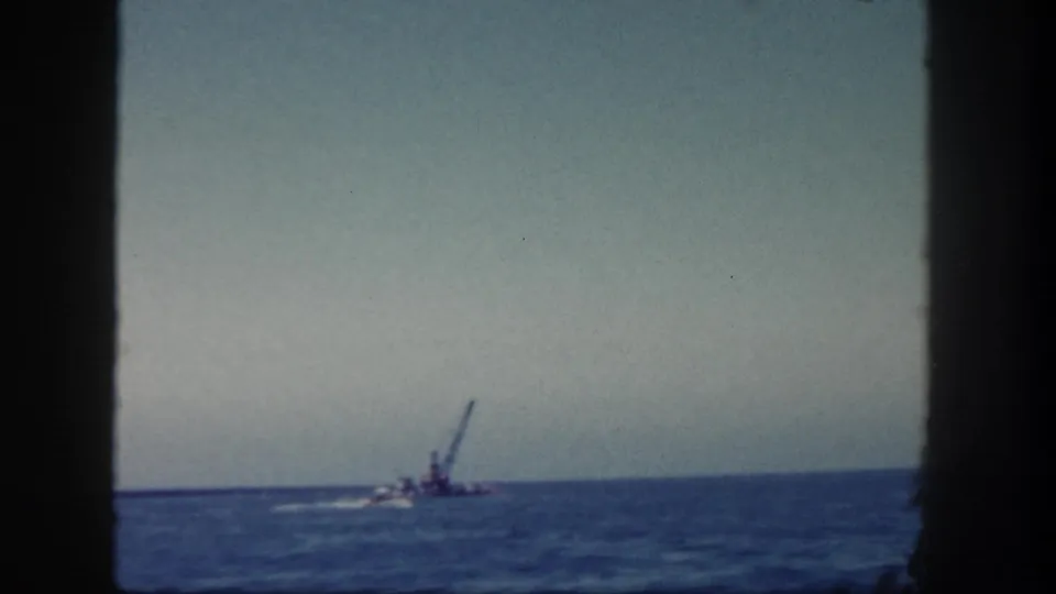 A 1962 San Diego 8mm frame shows the crane barge and a smaller boat far offshore, with wake lines against the blue water.