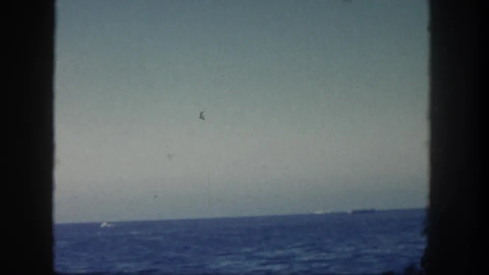 1962 San Diego 8mm frame showing blue ocean, pale sky, dark window-like edges, and small distant boats on the horizon.