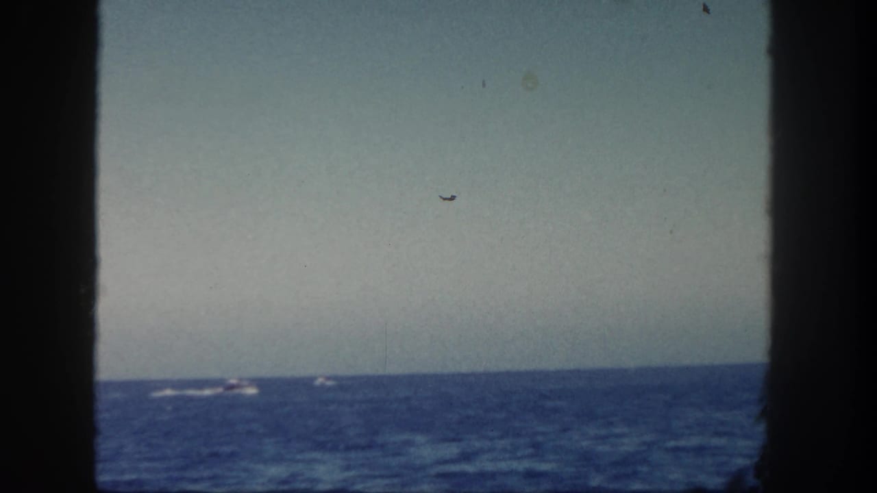 1962 San Diego coastal home-movie view across the water, with distant small boats and dark framing from the vessel or film gate.