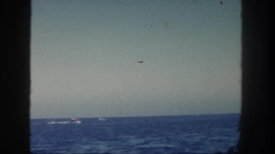 1962 San Diego coastal home-movie view across the water, with distant small boats and dark framing from the vessel or film gate.