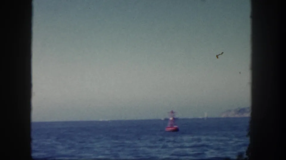 1962 San Diego 8mm frame showing open water, pale sky, a red buoy, distant horizon, and faint land at far right.