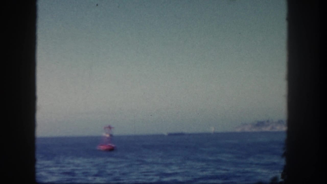 Red buoy near the horizon with open water, distant ship, and hazy coastline.