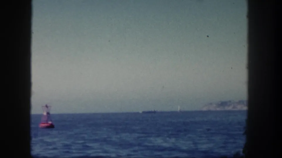 1962 San Diego 8mm frame with the red buoy shifted left, rippled blue water, distant vessel, and faint coastline in soft focus.
