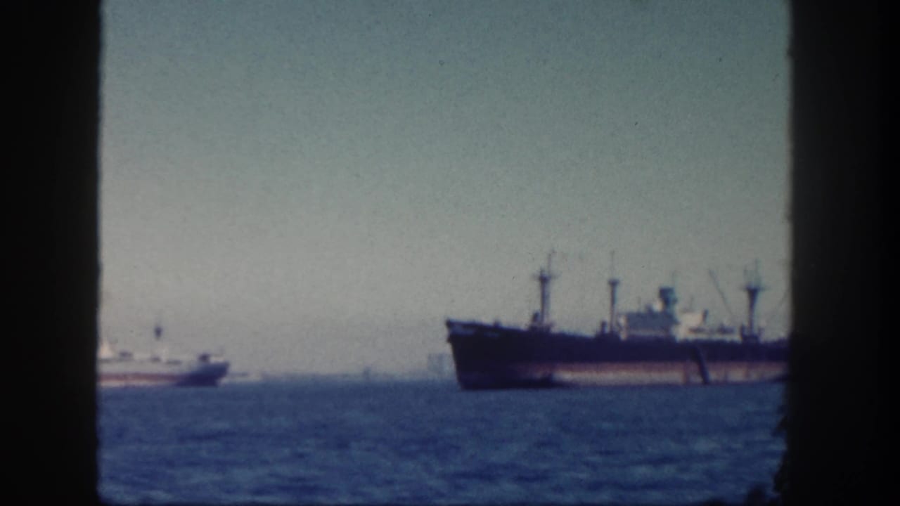 Large dark-hulled ship and smaller vessel on blue water under a hazy sky.