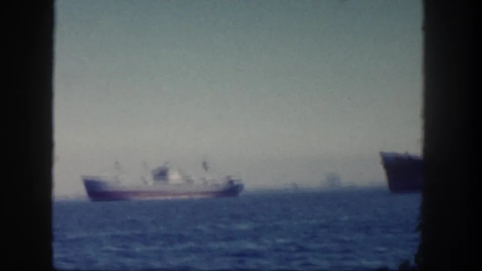 Soft 8mm frame from San Diego in 1962 showing a small vessel offshore, with part of a larger ship entering the right side.