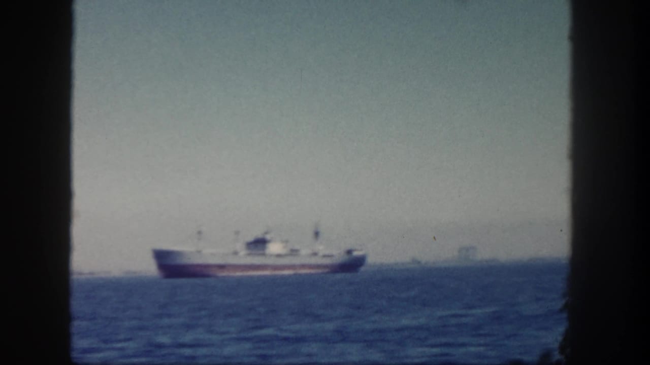 Cargo ship on blue water seen through dark window frames.