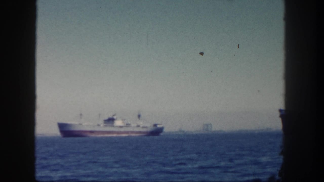 A cargo ship crosses San Diego waters in 1962, with a faint industrial shoreline visible through the haze.