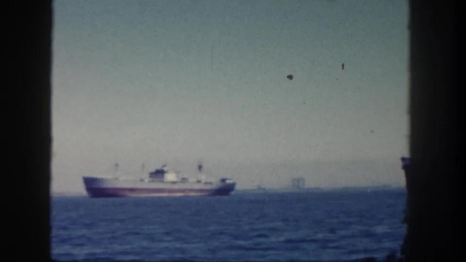 A cargo ship crosses San Diego waters in 1962, with a faint industrial shoreline visible through the haze.