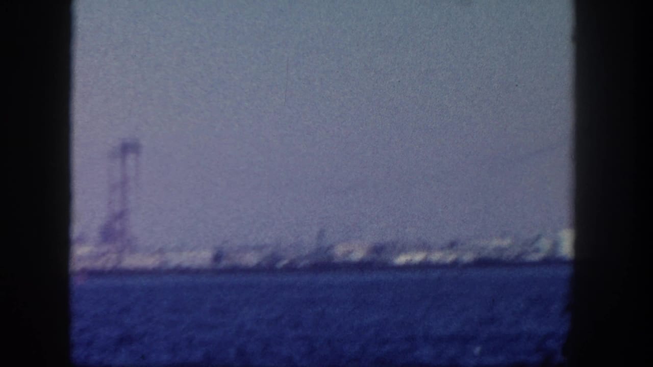 Distant waterfront and tall tower across blue water, framed by dark film edges.