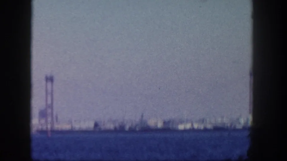 Soft 8mm footage of the San Diego waterfront shows a tall structure near the left edge and distant buildings across the water.