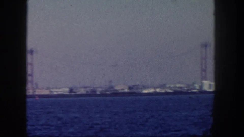A wide 1962 San Diego harbor view shows blue water, a low shoreline, and bridge-like towers along the distant horizon.