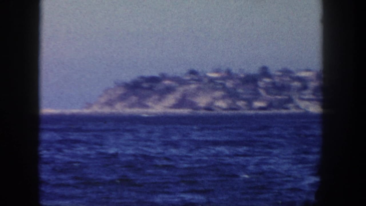 Hillside shoreline across blue water, framed by dark vertical film borders.