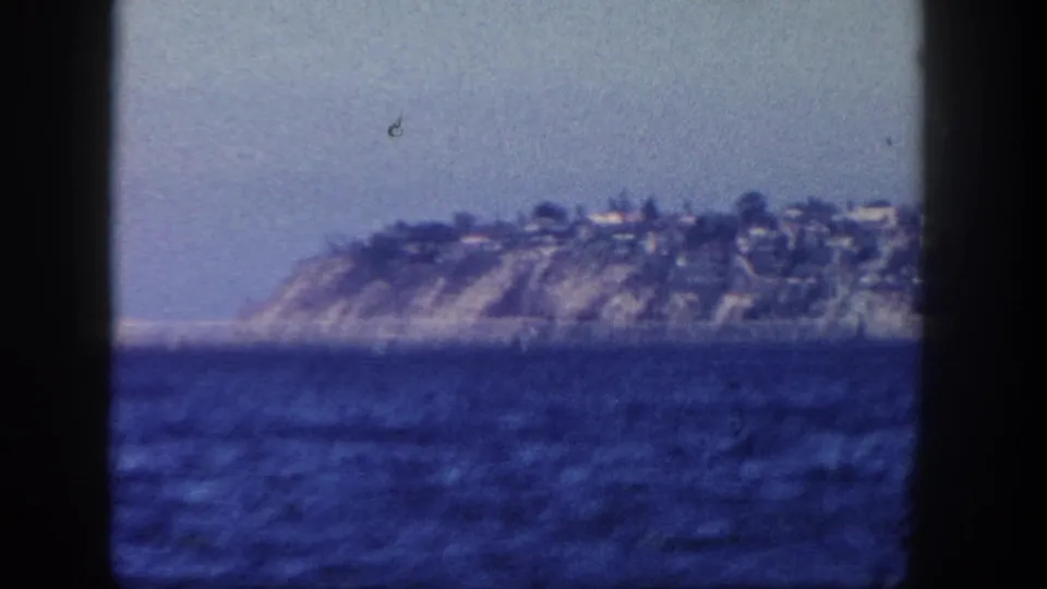 1962 San Diego coastal hillside across the water, with small distant buildings and a soft, grainy 8mm color image.