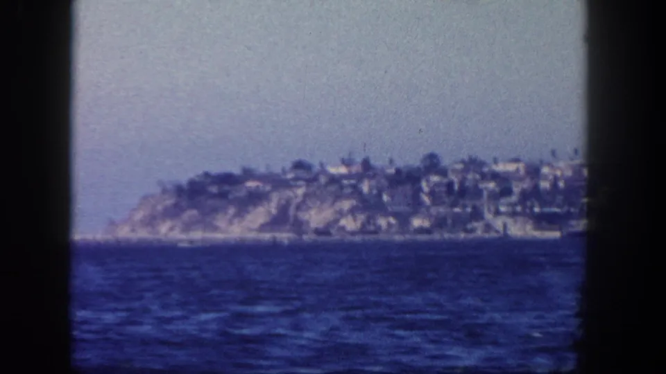 1962 San Diego shoreline from a boating excursion, showing blue water, a low hillside, and distant structures along the coast.