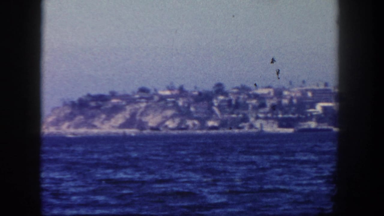 Distant cliffside shoreline with houses across blue water, framed by dark film edges.
