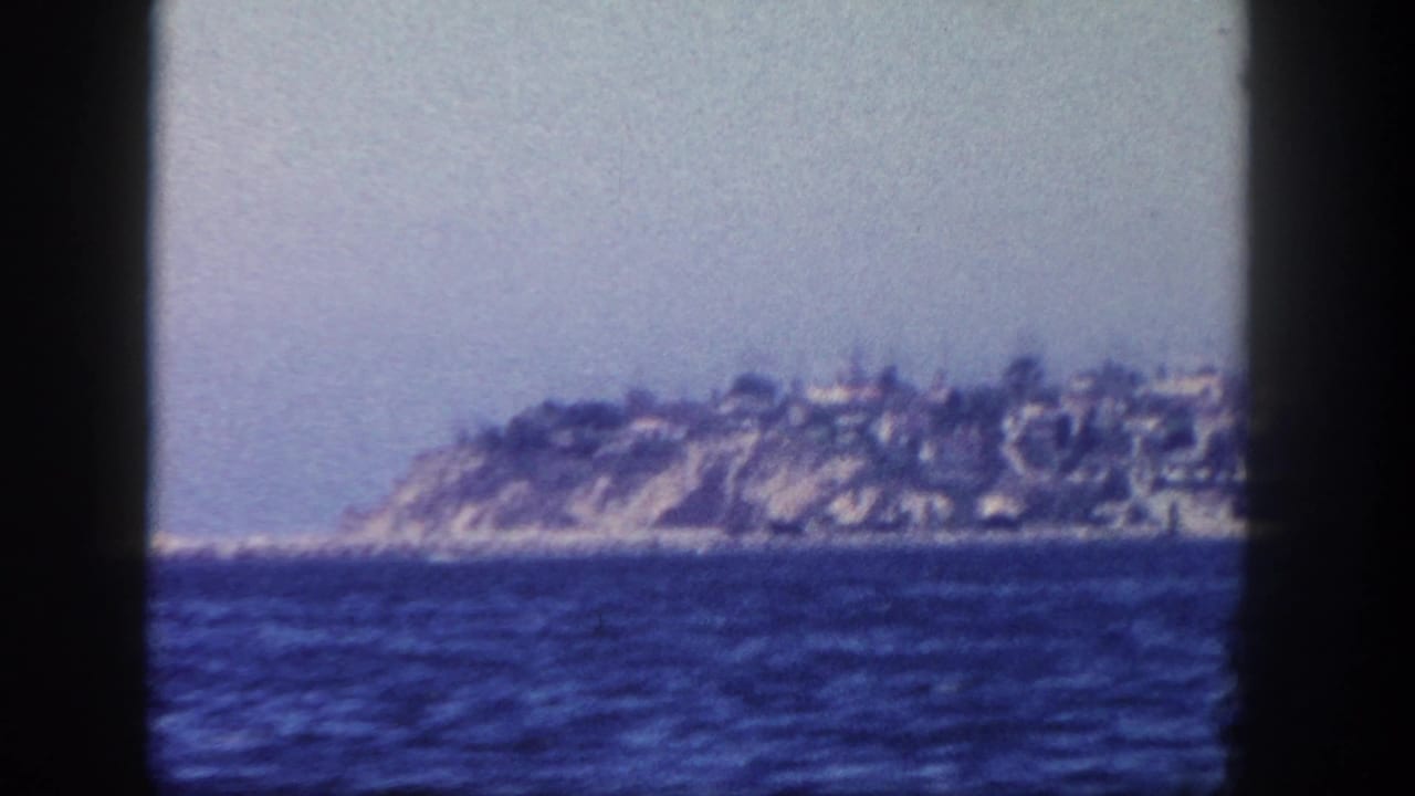 1962 San Diego-area 8mm frame showing a distant island or headland with cliffside houses across open water.