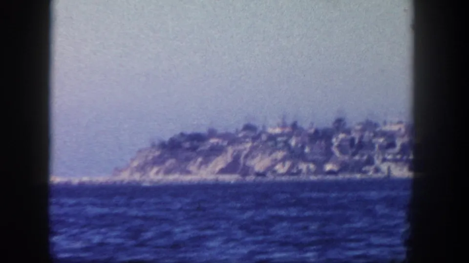 1962 San Diego-area 8mm frame showing a distant island or headland with cliffside houses across open water.