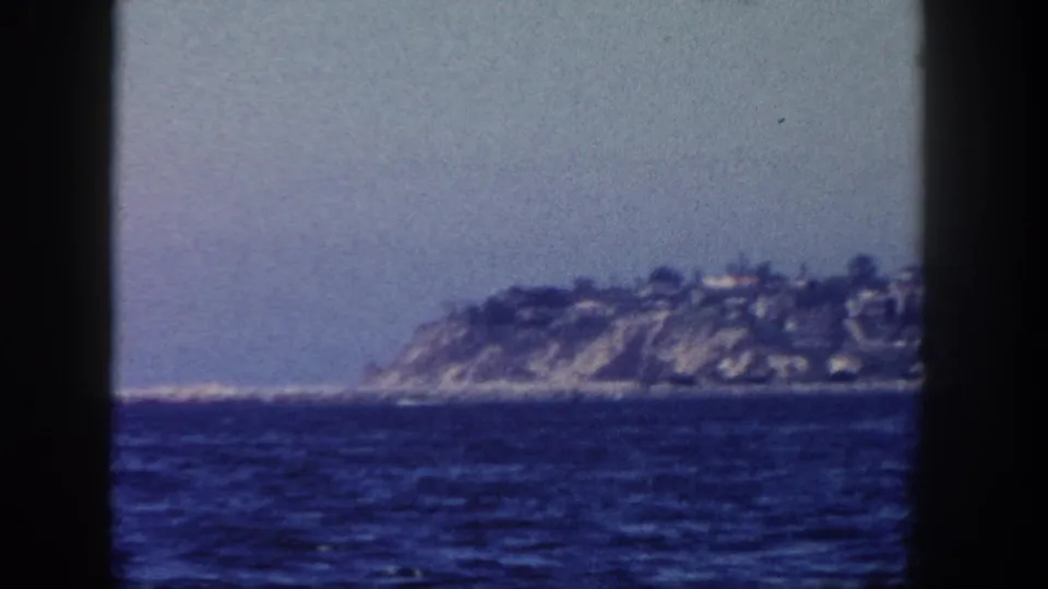 Soft 1962 San Diego-area boat view of a distant coastal headland with houses above the shoreline.