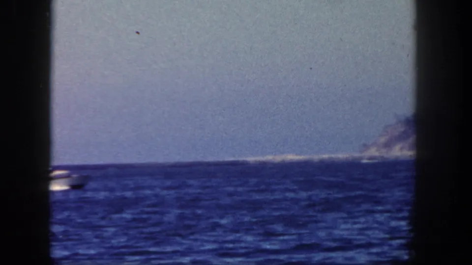 1962 San Diego-area 8mm frame with a small white motorboat on blue water and a distant shoreline at the right edge.