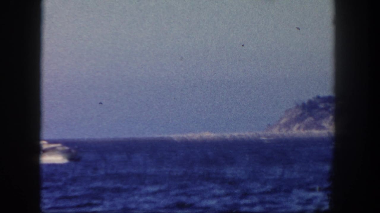 Motorboat on blue ocean with distant rocky shoreline and dark film borders.