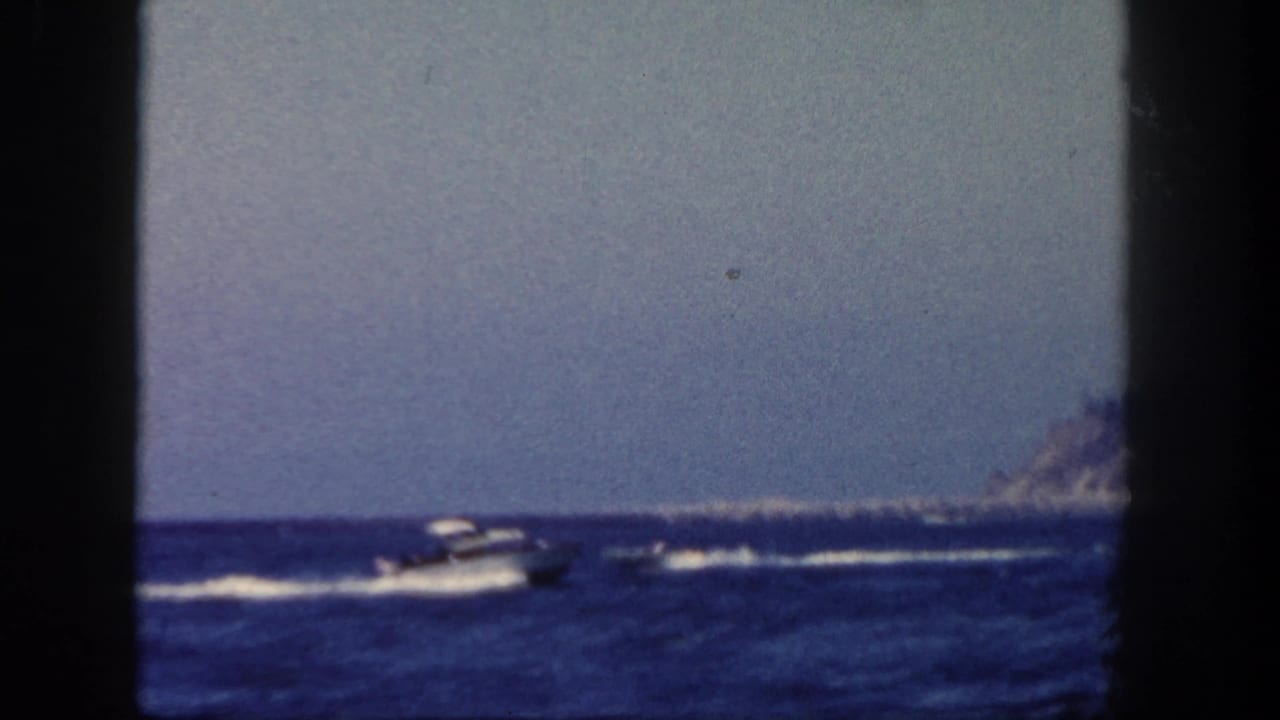1962 coastal home-movie view of motorboats leaving white wakes across blue water near a distant San Diego shoreline.