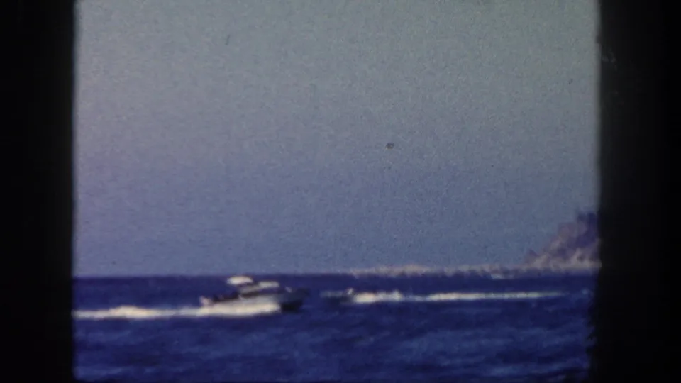1962 coastal home-movie view of motorboats leaving white wakes across blue water near a distant San Diego shoreline.