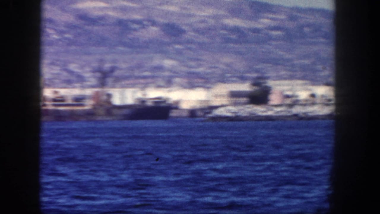 Distant San Diego shoreline and docked vessel across blue water with hills behind.