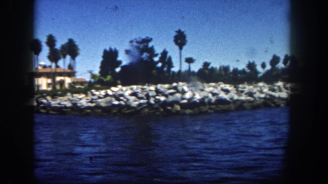 Rocky shoreline with a low stucco building, palm trees, and water in the foreground.