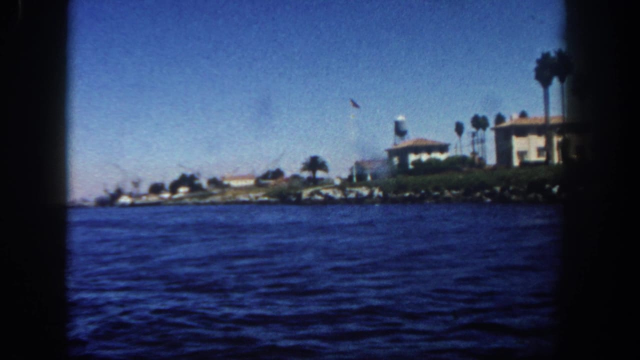 1962 San Diego coastline seen from a boat, with open water, shorefront buildings, palms, and a small flagpole.