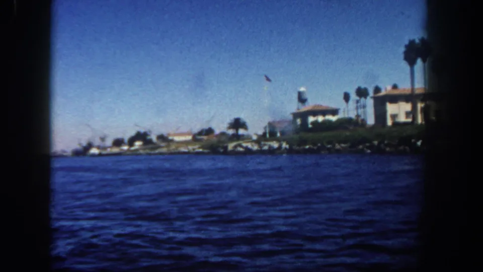 1962 San Diego coastline seen from a boat, with open water, shorefront buildings, palms, and a small flagpole.