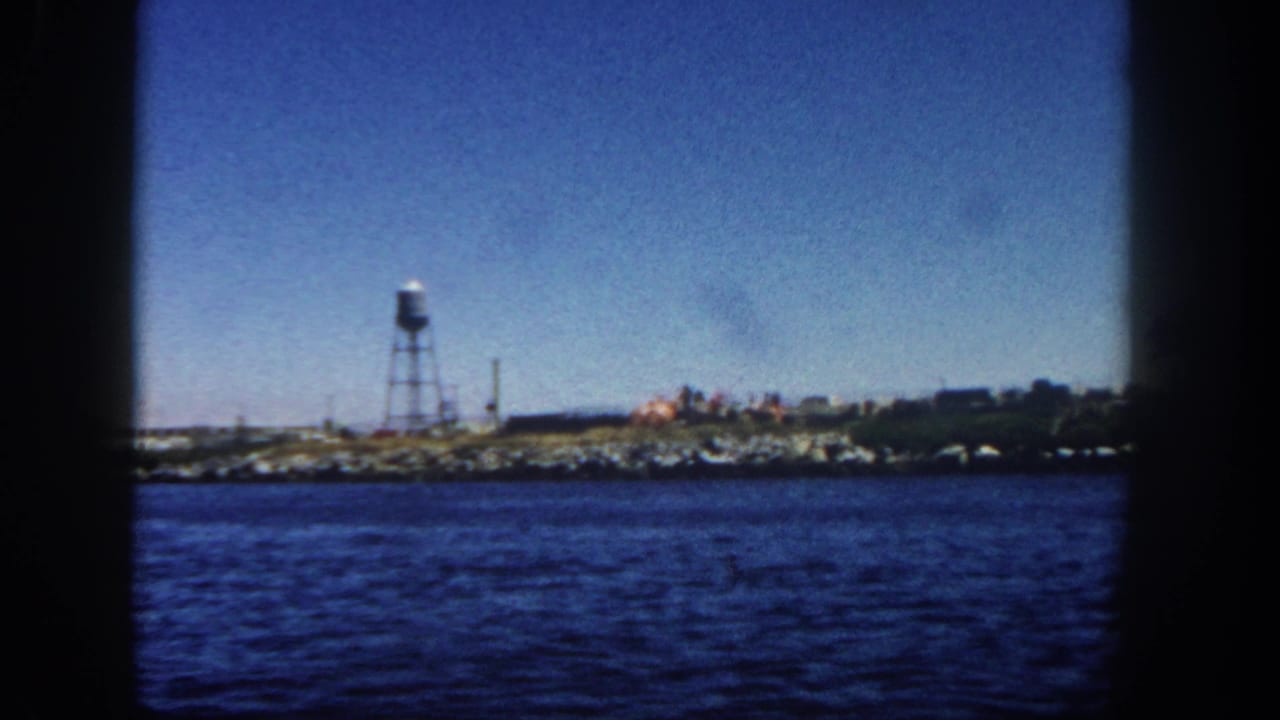 Rocky shoreline with a water tower seen across blue coastal water.