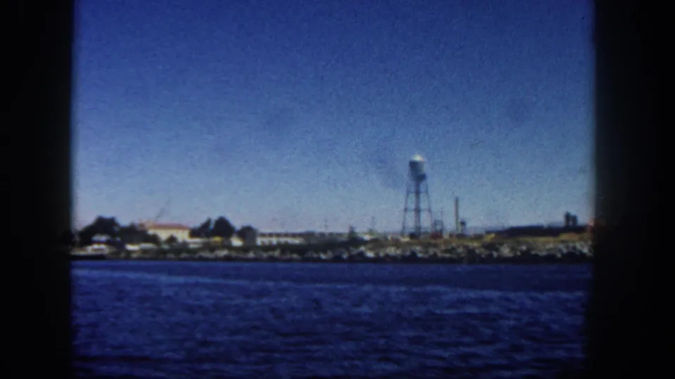 Soft 8mm view of San Diego shoreline from the water, showing low buildings, a water tower, and a dark vertical frame edge.
