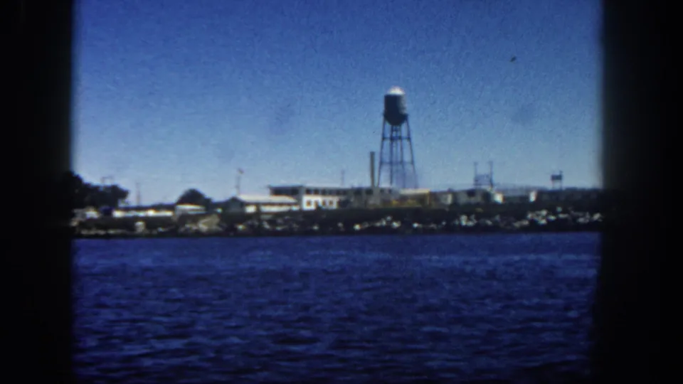 San Diego waterfront from the water with a tall water tower, low shoreline buildings, small masts, and saturated 8mm blue tones.