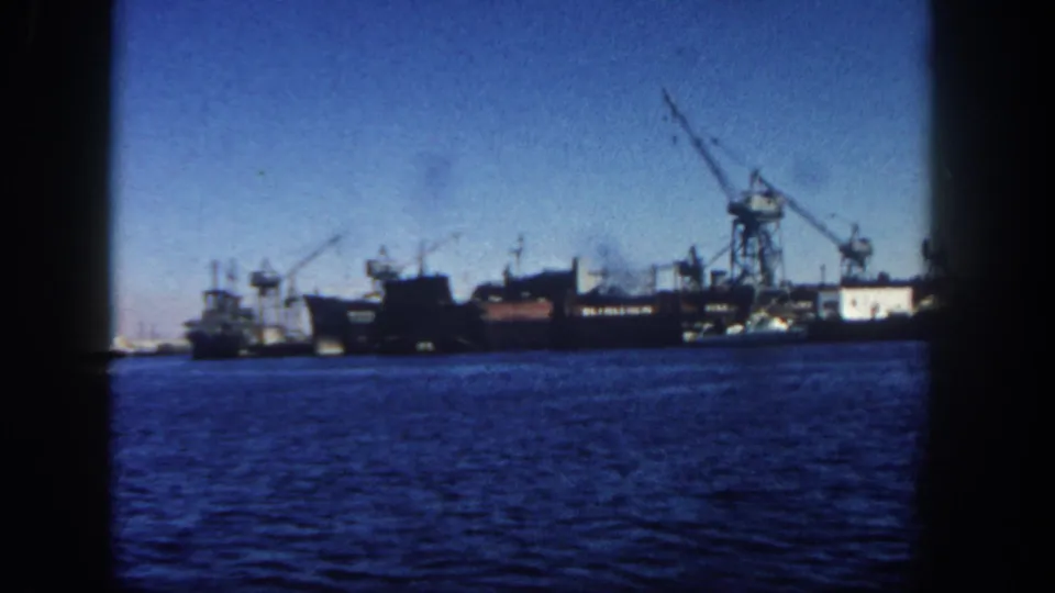1962 San Diego harbor footage shows a large ship beside cranes and a smaller vessel, with smoke rising above the industrial waterfront.