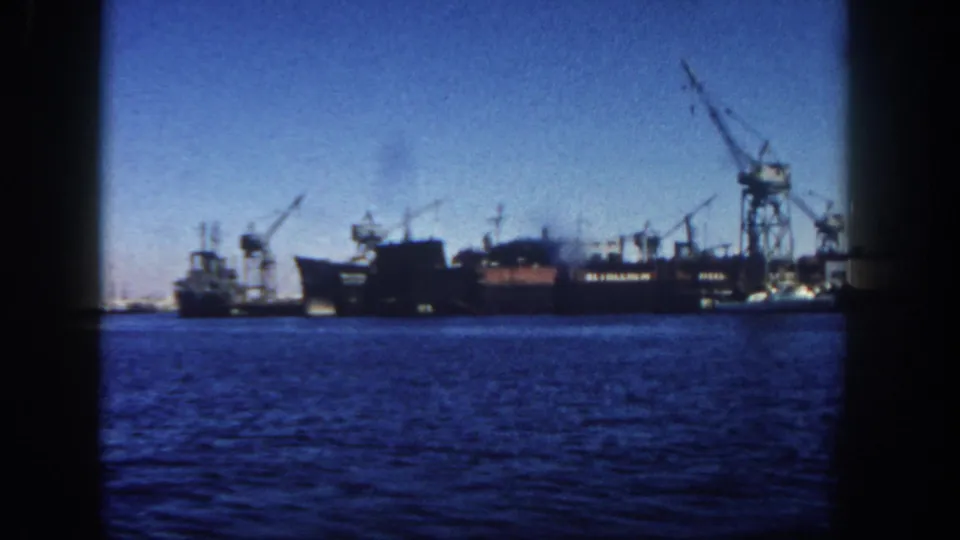 A 1962 San Diego seaport view holds on blue harbor water with ships, cranes, and waterfront structures in the distance.