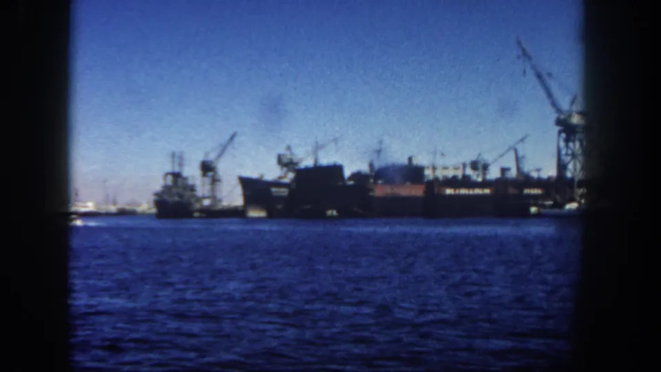 The frame shows San Diego harbor water with distant ships, dockside cranes, and a clear sky, recorded in soft 8mm color.