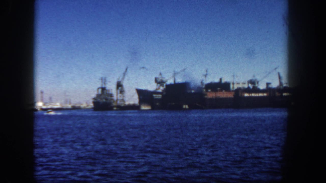 A distant 1962 San Diego port view shows boats and cranes along the waterfront beyond deep blue harbor water.