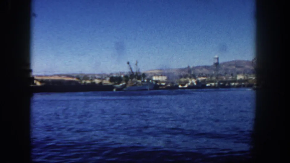 A wider 1962 San Diego harbor view shows boats, port cranes, waterfront buildings, and low hills beyond the water.