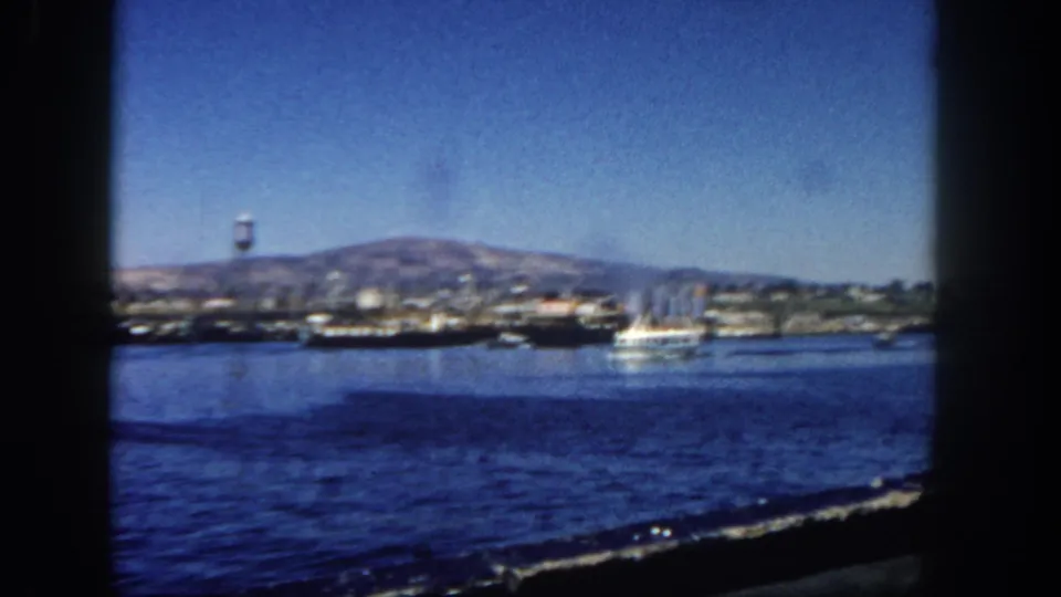 1962 San Diego Harbor footage showing docked vessels, a water tower, a small boat on the water, and mountains behind the port.