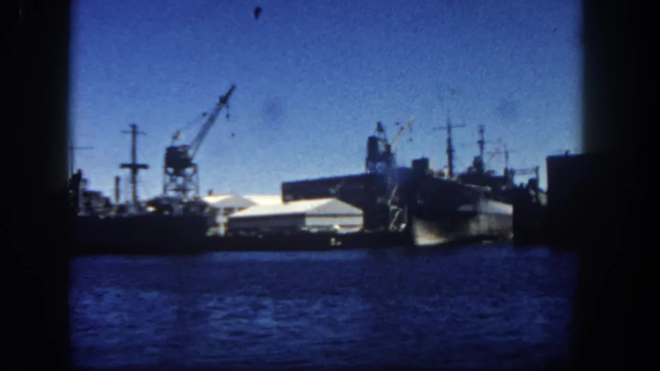 1962 San Diego Harbor view with larger docked vessels, cranes, industrial waterfront structures, and dark film framing.