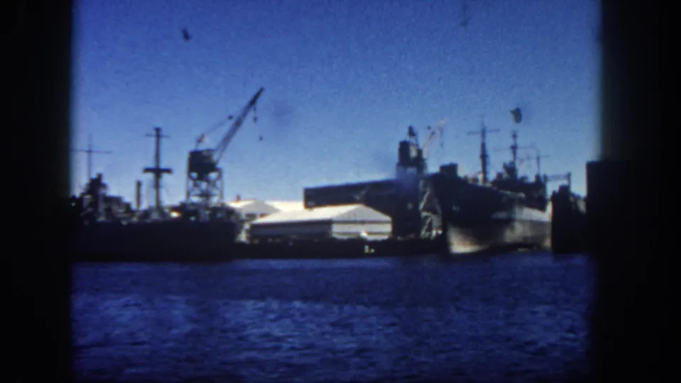1962 San Diego harbor view showing docked naval or cargo ships, pier structures, and heavy cranes across the water.