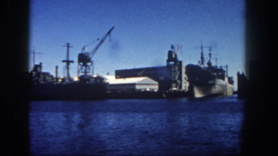 1962 San Diego harbor frame with moored ships, crane silhouettes, pier buildings, and dark 8mm gate edges.